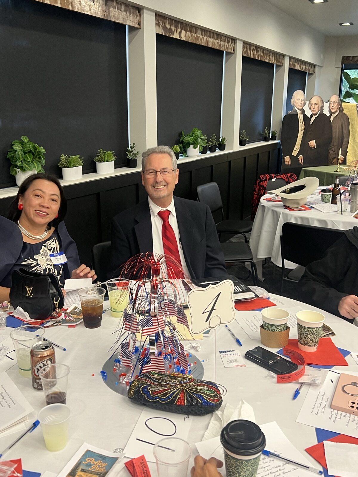 Keynote speaker Dan Happel and a guest smile at table 4, with a patriotic centerpiece and Founders cutouts in the background.